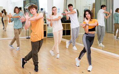Group of teenage dancers practicing synchronous vigorous dance in modern studio