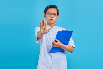 Angry male nurse holding clipboard and doing stop gesture with palms on blue background