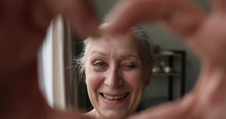Closeup portrait smiling aged granny make video call to beloved family look at web camera in finger heart mean love. Thankful hoary senior adult lady vlogger influencer express gratitude to audience