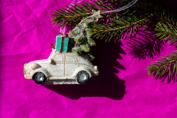 White toy truck car with green Christmas pine tree and blue gift box on a roof on a bright fuchsia background. Happy 2022 New Year's Eve. Greeting card, copy space. Gifts delivery. Contrasting shades.