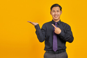 Fototapeta premium Cheerful young handsome businessman showing copy space on palm on yellow background