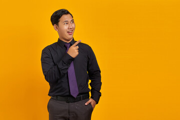 Smiling young Asian man pointing fingers at copy space on yellow background