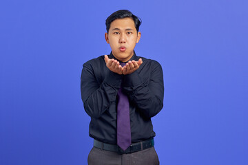 Portrait of charming young Asian man hold hand palms send air kiss on purple background