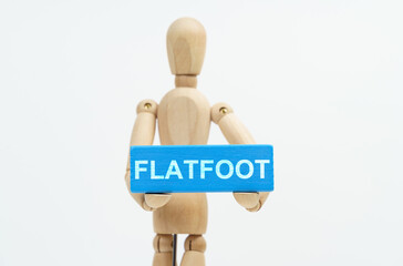 A figurine of a man holds in his hands a blue wooden block with the inscription FLATFOOT. The figurine is out of focus.