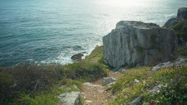 4K Cinematic shot of a coastal foot path going down hill to the edge of a cliff, on a sunny day, on the island of Portland, in Dorset, England.