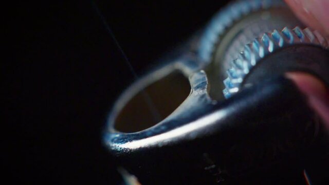 Super slow motion extreme macro shot of a lighter being lit in the dark, with a flame coming out, from the side.