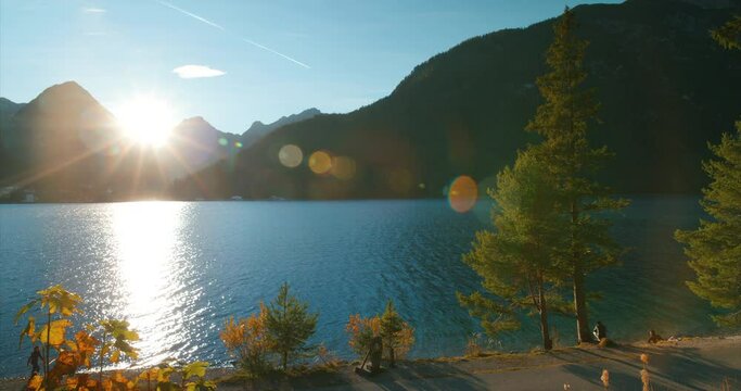 People by trees  near walking trail by scenic view of alps mountains at lake achensee in sunset golden hour in Austria, Europe. Wide Angle.
