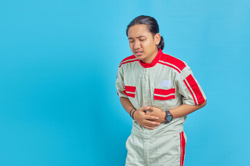 Portrait of handsome mechanic in pain with hand on stomach on blue background