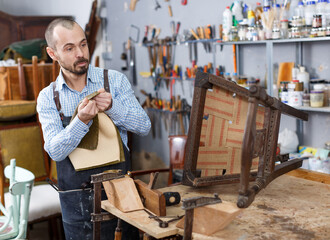 Professional furniture restorer in process of renovation vintage armchair in workshop