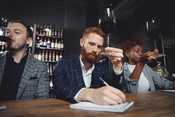 Friends tasting red wine sommeliers and taking notes at degustation notepad