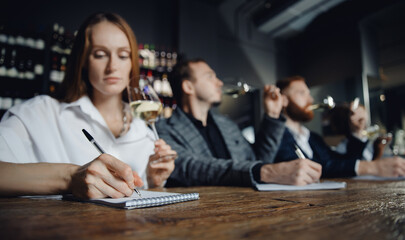 Sommeliers female and male tasting white wine and making notes at degustation card notepad