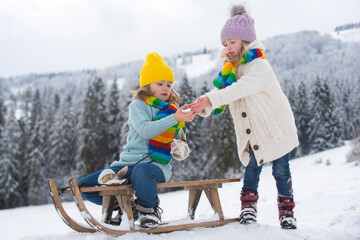 Boy and girl kids sliding with sledge in the snow. Active winter children outdoors. Kids playing in the winter forest.