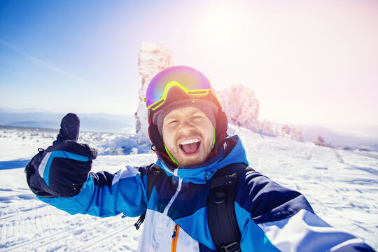 Smile man skier makes selfie photo on background of snowy forest in mountains. Winter recreation on nature ski tour
