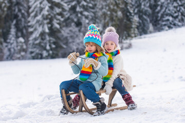 Fototapeta na wymiar Children on sleigh. Kids boy and girl plays outside in the snow. Winter, holiday and Christmas time. New Year wallpaper, Christmas greeting card.