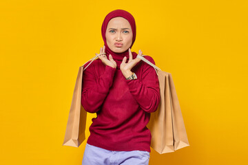 Portrait of beautiful excited Asian woman holding shopping bags on yellow background