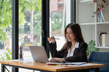 Professional asian woman at work. Shot of a financial consultant businesswoman working on laptop and doing some paperwork at the office