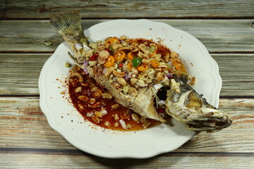 Traditional deep fried whole seabass fish seasoning with spicy mixed herbal and chilly serving on the plate. 