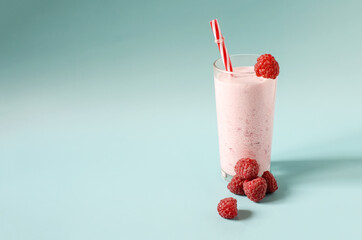 Milkshake in a transparent glass with raspberries and a red tube on a blue background close-up. Cocktail of ice cream, milk and berries on a colored background copy space