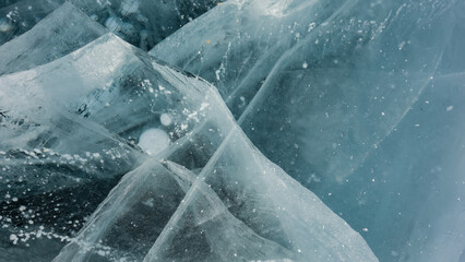 Turquoise transparent ice of a frozen lake. Close-up. Full screen. Deep cracks, bubbles of frozen methane gas are visible. Baikal