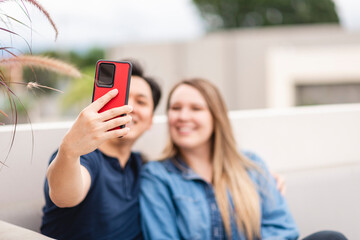 asian man with a cell phone in his hand taking a picture with his caucasian girlfriend outdoors