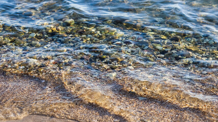 Background of sandy, stones and flowing waves on the sea beach. Summer holidays and coastal nature concept