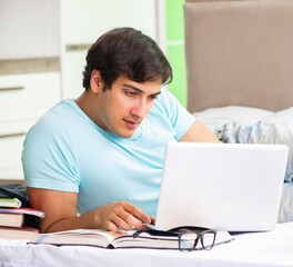 Student preparing for exams at home in bedroom lying on the bed