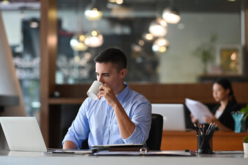 Smart businessman drinking coffee and using laptop computer in office.