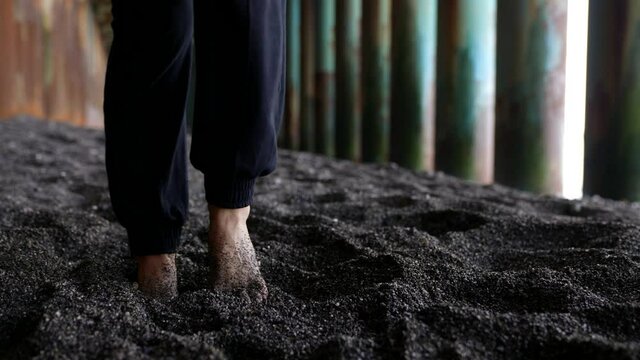 close-up of bare legs in dark trousers. feet trample in the coarse black sand against the background of the bridge pillars. the camera is moving