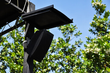 Mini speaker of the outdoor stage installed on the black metal pole which has metal roof above to protect it from the rain. - obrazy, fototapety, plakaty