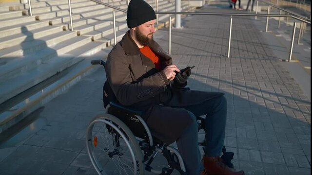 disabled man in wheelchair is waiting help in front of stair in city, sending message in smartphone