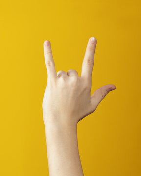 hand showing rock and roll gesture on yellow background. Hand makes goat gesture.