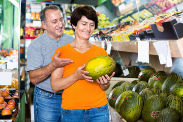 Fototapeta premium Adult happy cheerful positive male and female are choosing green melons in the store.
