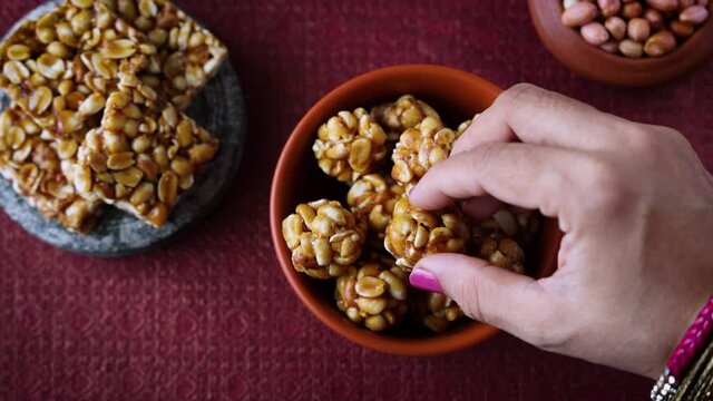 Peanut chikki ladoo laddu candy Kadalai mittai woman hand serving winter food Indian festival snack sweet 4K video footage Lohri Makar Sankranti Pongal Diwali harvest festival Tamil Nadu Punjab India