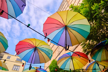 Fototapeta na wymiar Lots of rainbow-colored umbrellas and lightbulbs hanging above street. Decoration of streets made of umbrellas