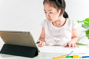 Asian adorable little kid toddler girl using a tablet mobile to online e-learning class learning from home while school closed during lockdown from coronavirus outbreak. The Home study child concept