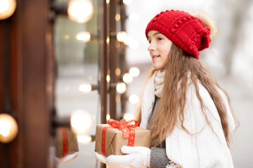 A sweet young girl with a gift looks out the shop window. New Year. Christmas. Atmosphere.