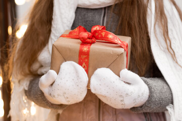 A sweet young girl with a gift looks out the shop window. New Year. Christmas. Atmosphere.
