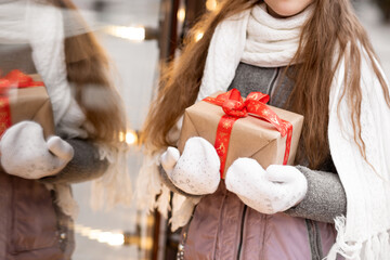 A sweet young girl with a gift looks out the shop window. New Year. Christmas. Atmosphere.