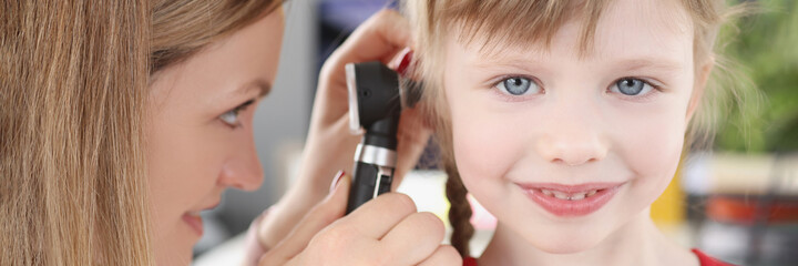 Woman pediatrician looking at eardrum of little girl using otoscope in clinic
