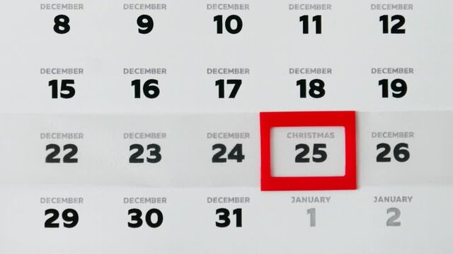 A beautiful December page of the wall calendar and a male finger moves a red cursor to Christmas date close-up