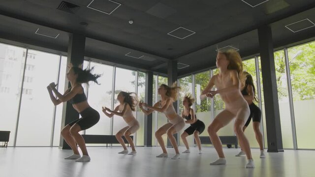 Fitness classes for young ladies. Group of young sporty women exercising with coach, practicing jump squats together