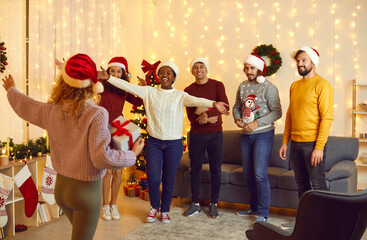 Group of young multiracial friends in santa hats welcoming their female friend at Christmas party...