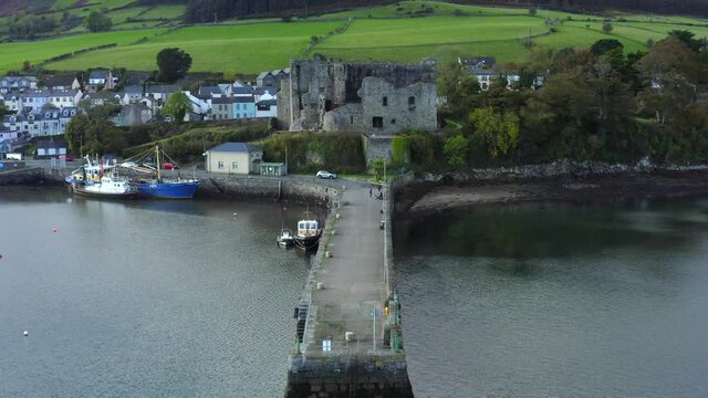 King John's Castle, Carlingford, Louth, Ireland, October 2021. Drone pushes towards the castle along the harbour pier with fishing boats and the town in the background.