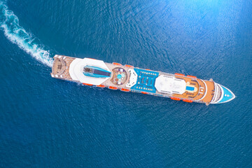 Cruise liner ship turns in ocean with blue water. Aerial top view.