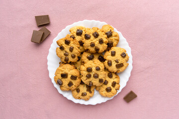 Homemade cookies with chocolate chips on pink textile background, top view