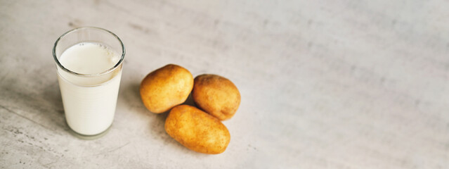 A transparent glass with potato milk on the table next to the potato tubers. 