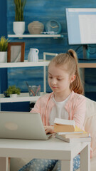 Little child using laptop for online school classes at home. Schoolgirl looking at display of modern device for homework and remote education. Young pupil learning courses on internet