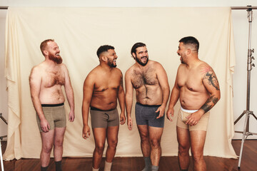 Four shirtless men laughing cheerfully in a studio