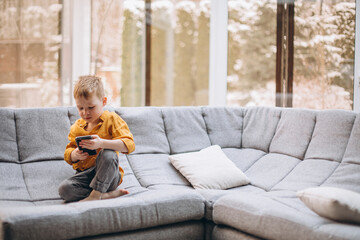 Cute little boy sitting on sofa and using phone