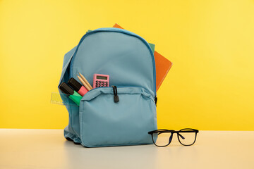 Backpack with different colorful stationery and glasses on a table. Back to school theme